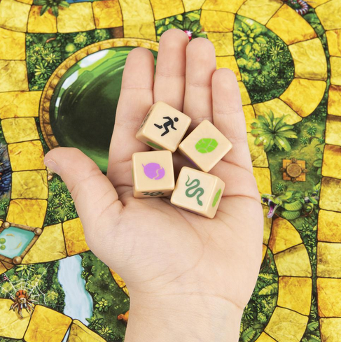 Hand holding four custom dice with symbols over Jumanji board game path and green dome in the center.