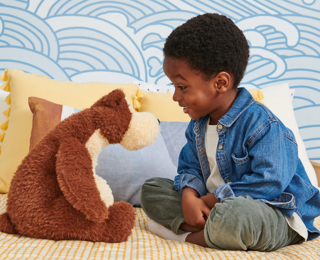 Teddy Bear Goober sitting upright with soft chocolate and vanilla plush, facing a smiling child on a bed.