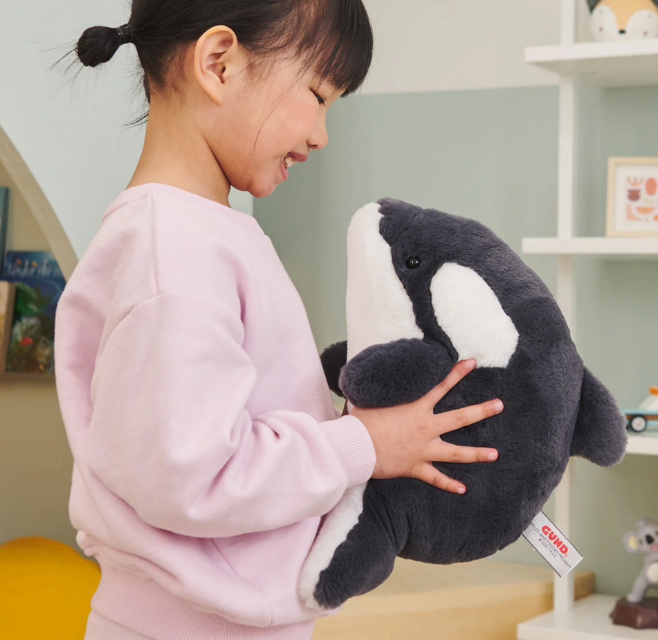 Child smiling and hugging the soft plush Snuffles Orca Flynn with black and white design.