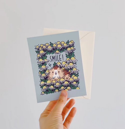 Hand holding a Guinea Pig Smile! Card featuring a smiling guinea pig surrounded by white flowers and a matching ivory envelope.