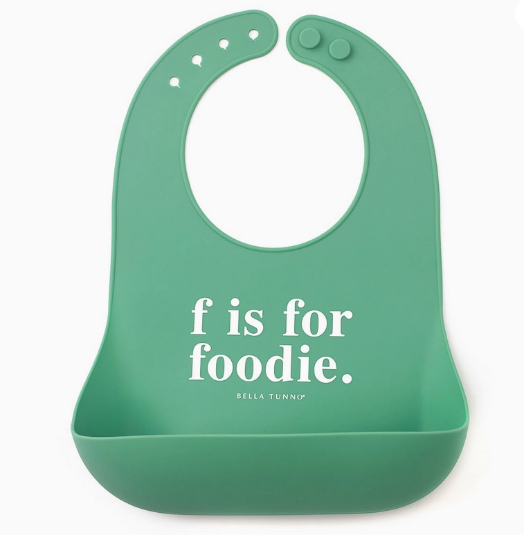 Green silicone bib with adjustable snaps and pocket featuring the phrase "f is for foodie" in white text