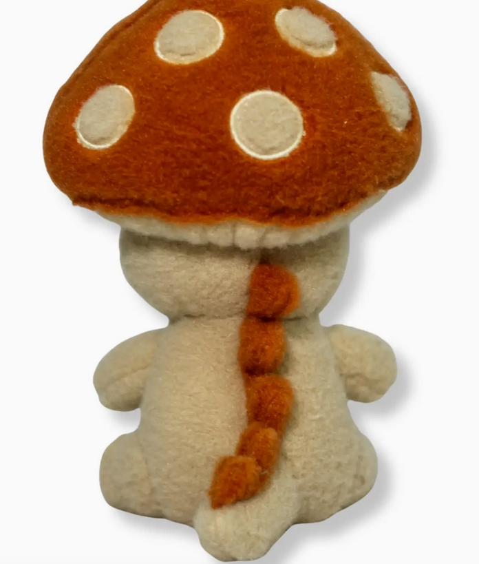 Plush mushroom character with orange cap and white spots viewed from behind showing small arms and tail details