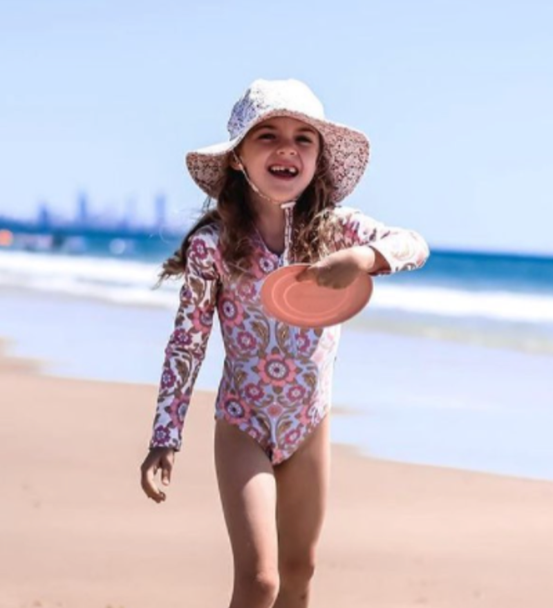 Young girl playing on the beach holding a pink Scrunch Flyer Duck Egg Blue made of soft, durable silicone.