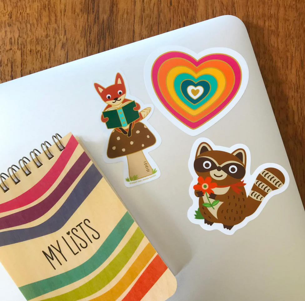Go Wild Raccoon Sticker Birthday Card featuring a raccoon with a flower on a laptop with colorful stickers and a notebook.