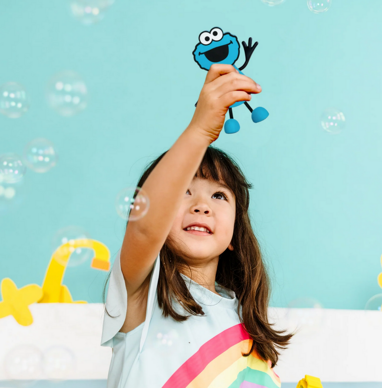 Young girl holding up the Glo Pals Cookie Monster Character toy against a blue background with bubbles.