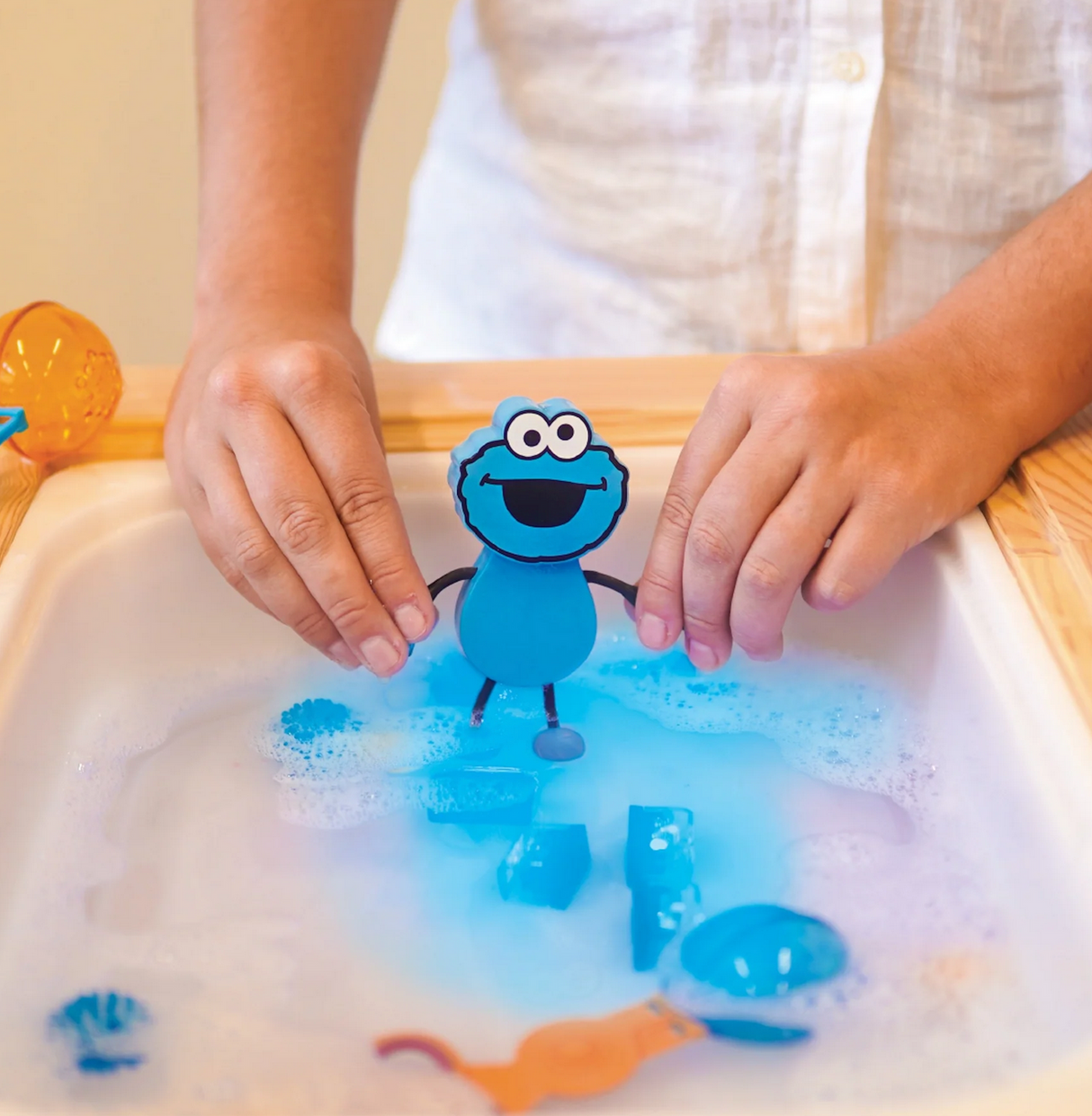 Hands holding the Glo Pals Cookie Monster Character glowing blue in water with foam and toys around.