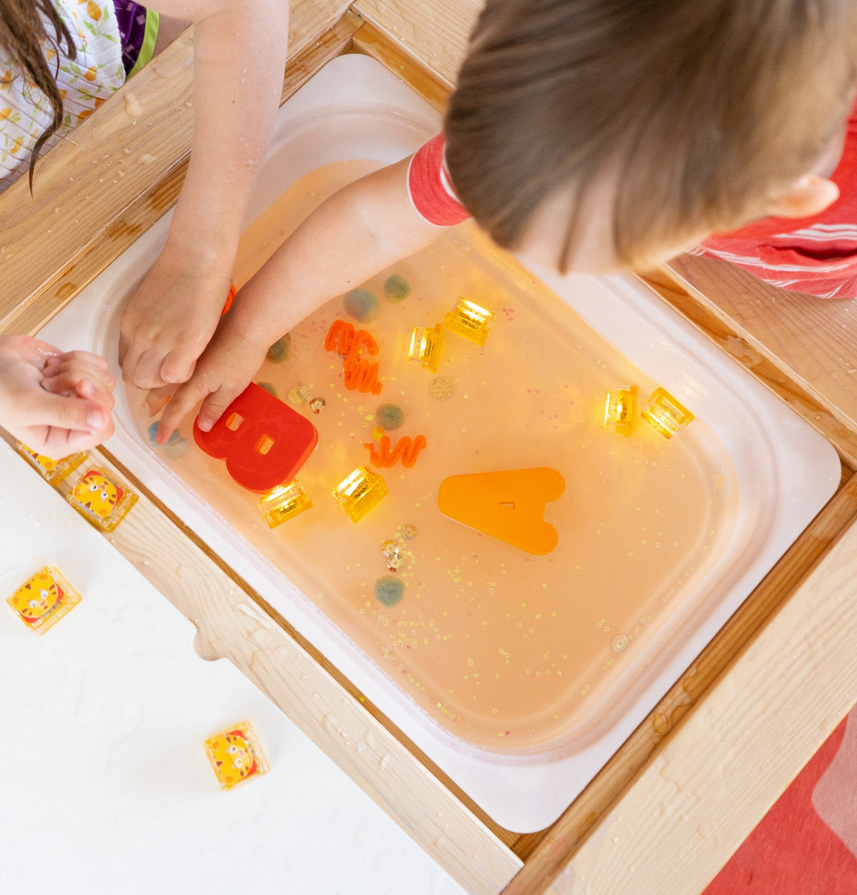 Children playing with glowing cubes and letters in water with Glo Pals Daniel Tiger's Neighborhood light-up toys.