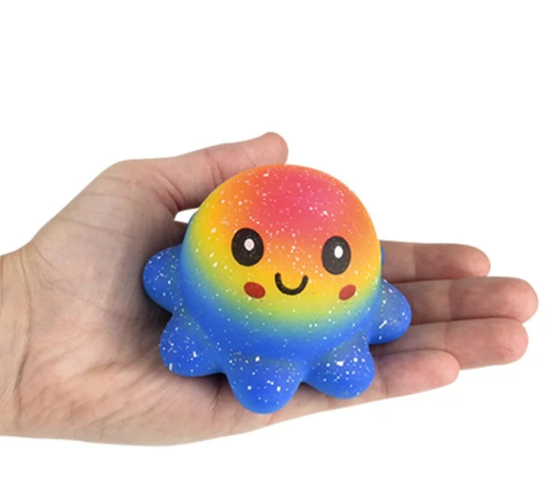 Hand holding a colorful Squish & Stretch Rainbow Octopus toy with a smiling face and speckled design.