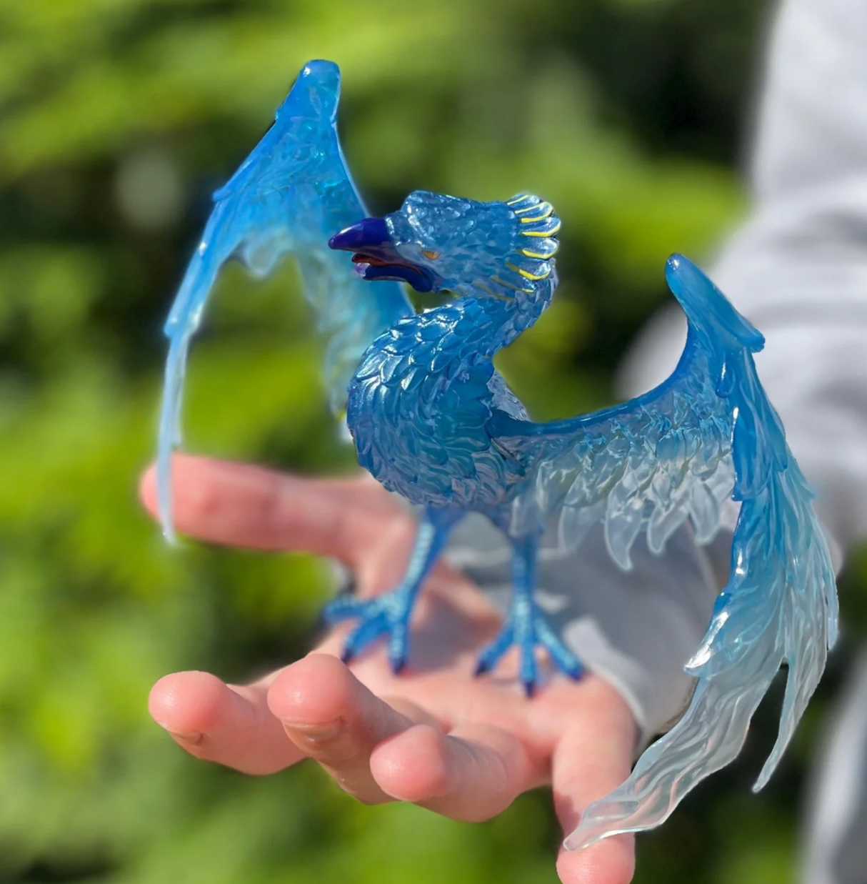Blue Phoenix toy figure with translucent blue wings and detailed feathers, held in hand outdoors.
