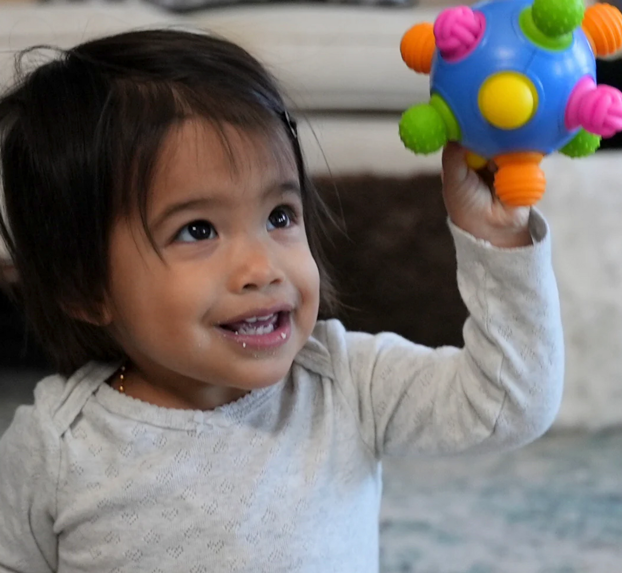 Toddler happily holding and playing with a colorful Woblii Sensory Ball with textured push and pull nubs.