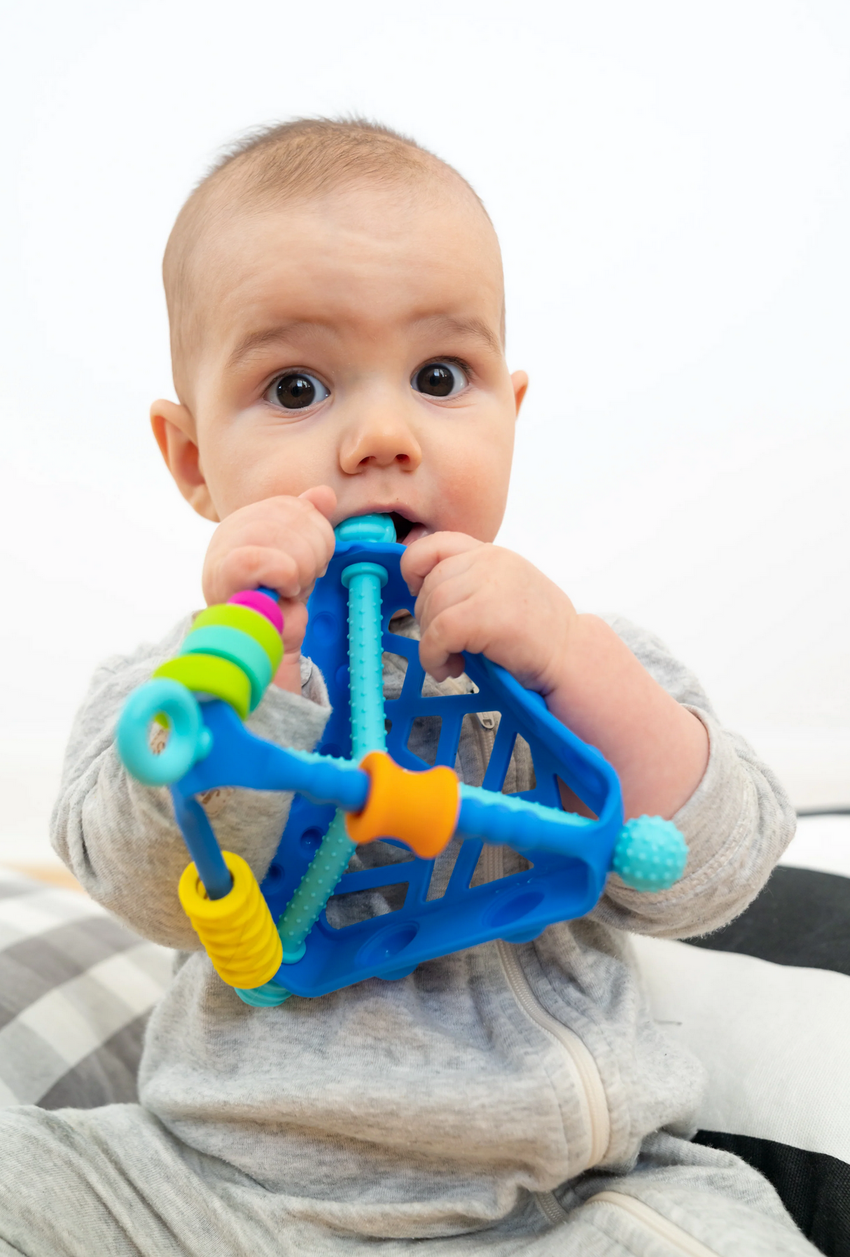 Baby chewing on a blue Wigloo Activity Toy with multiple textures and sensory features, designed for ages 6 months and up.