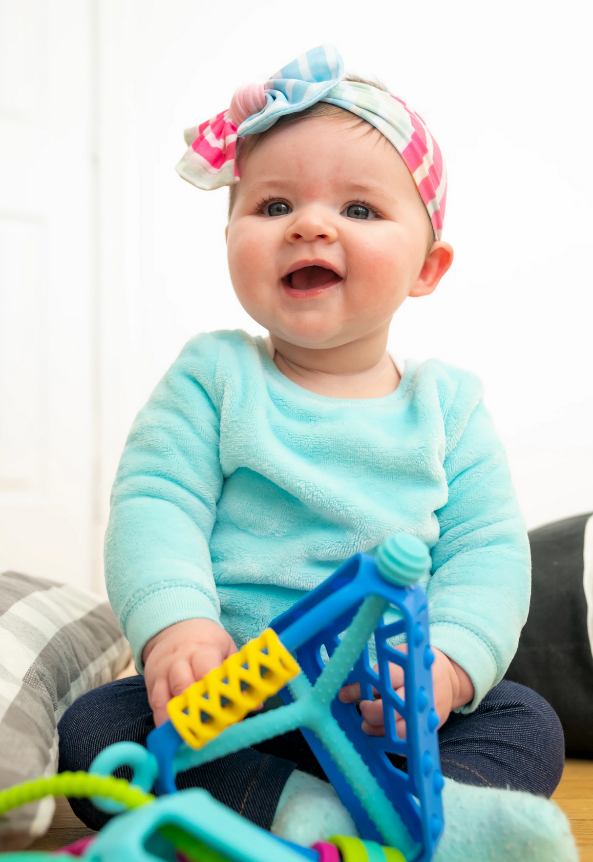 Baby smiling while playing with the colorful Wigloo Activity Toy featuring silicone bubbles and springy cords.