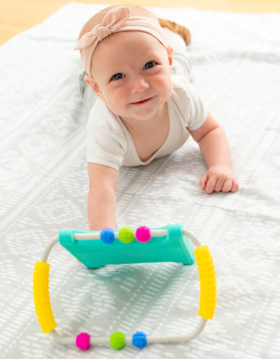 Baby lying on tummy reaching for Peeka Developmental Mirror with colorful beads and yellow grips.