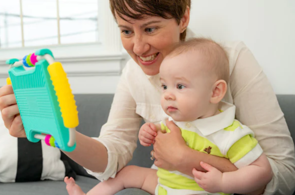 Peeka Developmental Mirror held by smiling adult engaging baby in bright room during tummy time play.