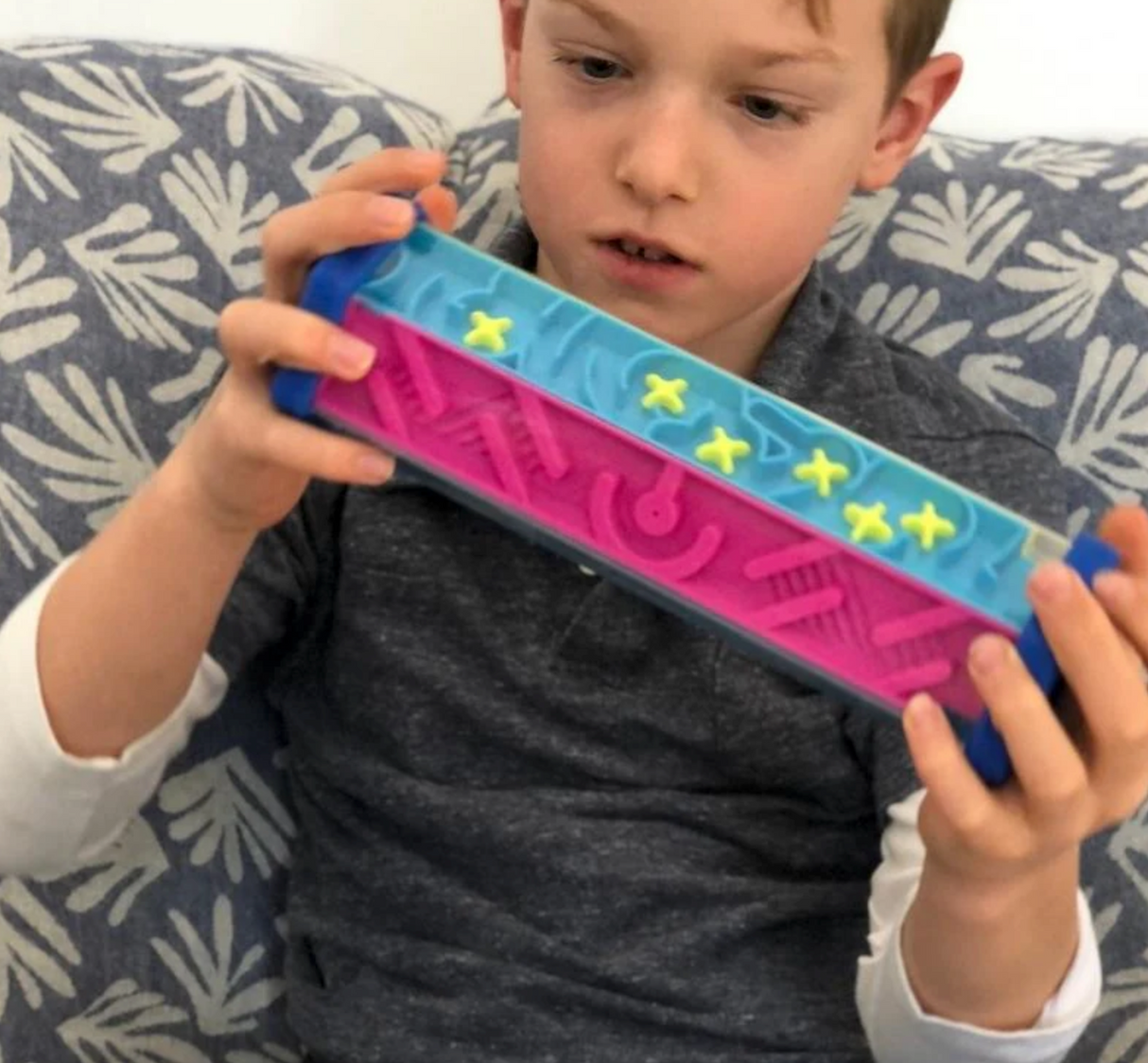 Child focused and engaged playing with Zoomi The Hexagon Maze puzzle with colorful panels and yellow ball.
