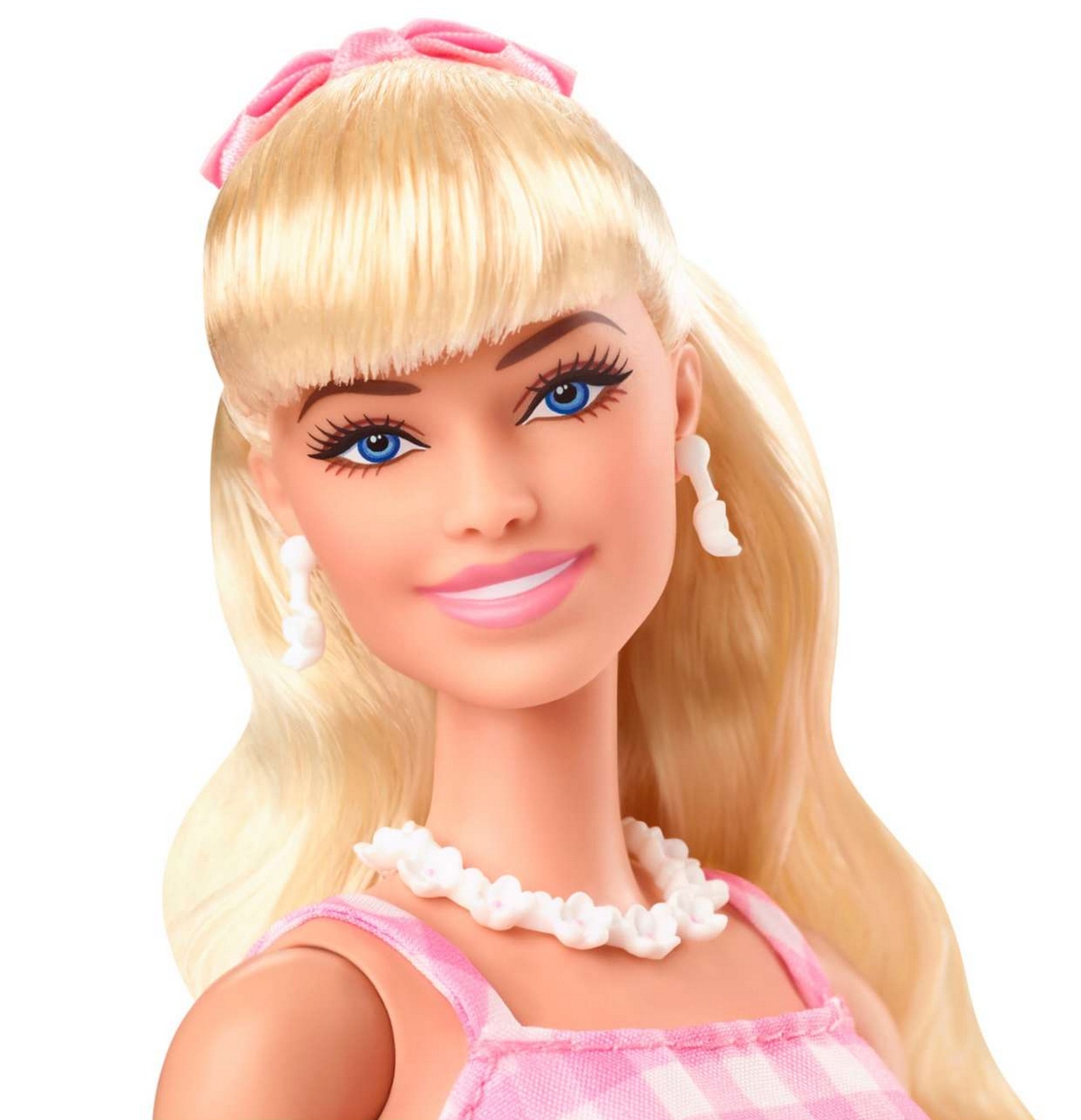 Barbie The Movie doll with blonde hair, pink gingham dress, daisy necklace, and pastel bow accessory smiling.