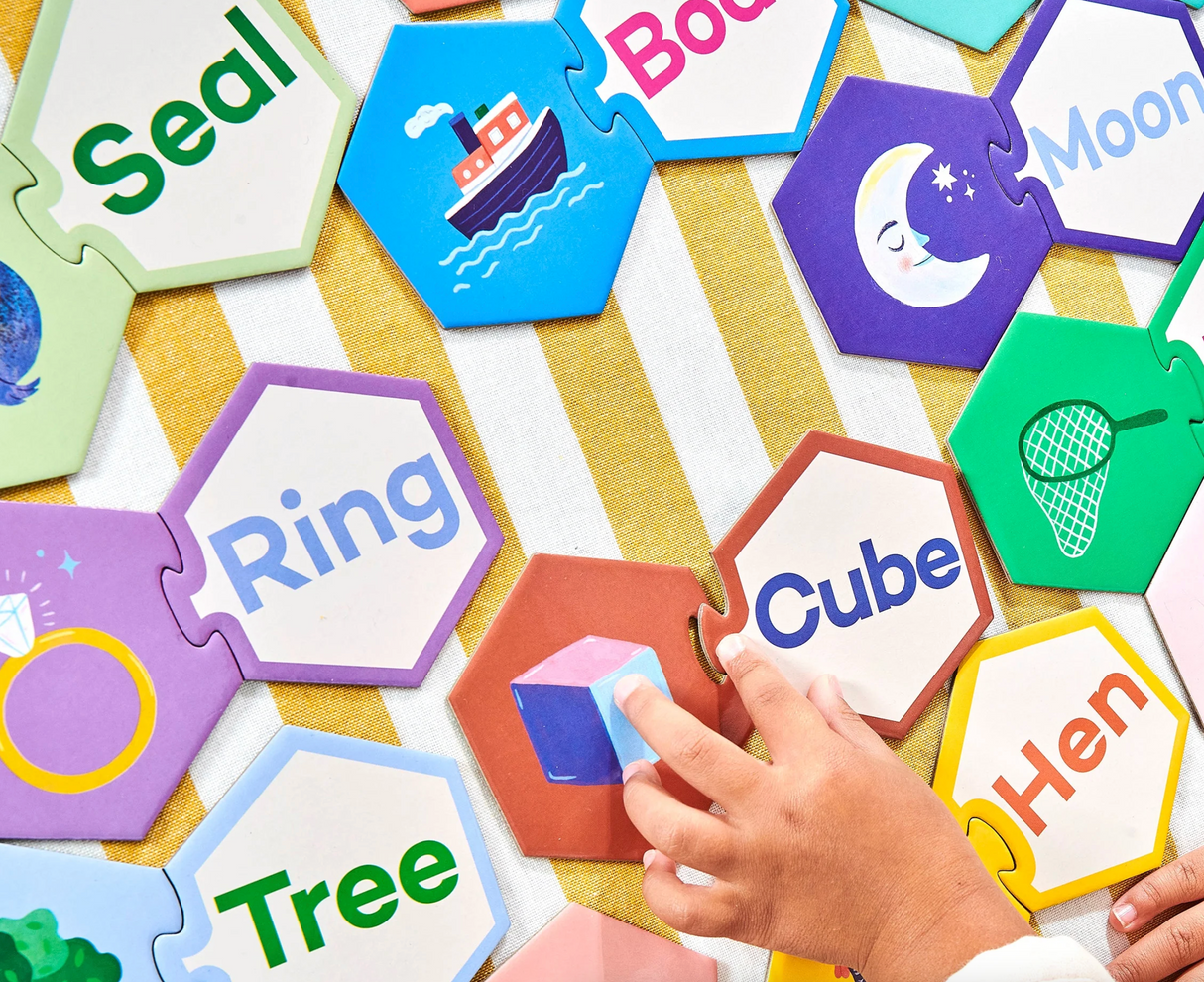 Child’s hand connecting colorful hexagon puzzle pieces with words and images in Simple Words Puzzle Pairs educational set.