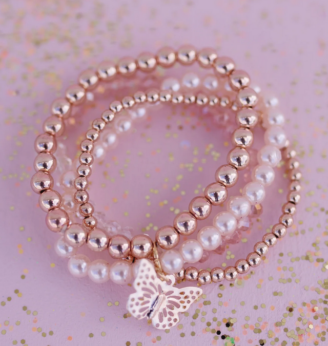 Blush Crush Bracelets featuring four strands of pearls and gold beads with a gold butterfly charm on pink background.