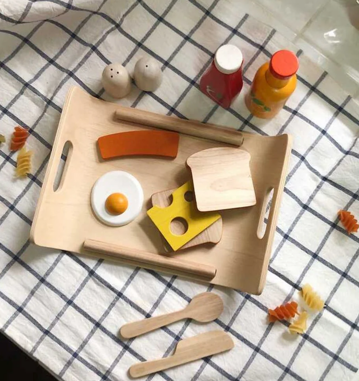 Breakfast Menu wooden play set with bread, cheese, egg, sausage, salt, pepper, tray, and play utensils on cloth background.