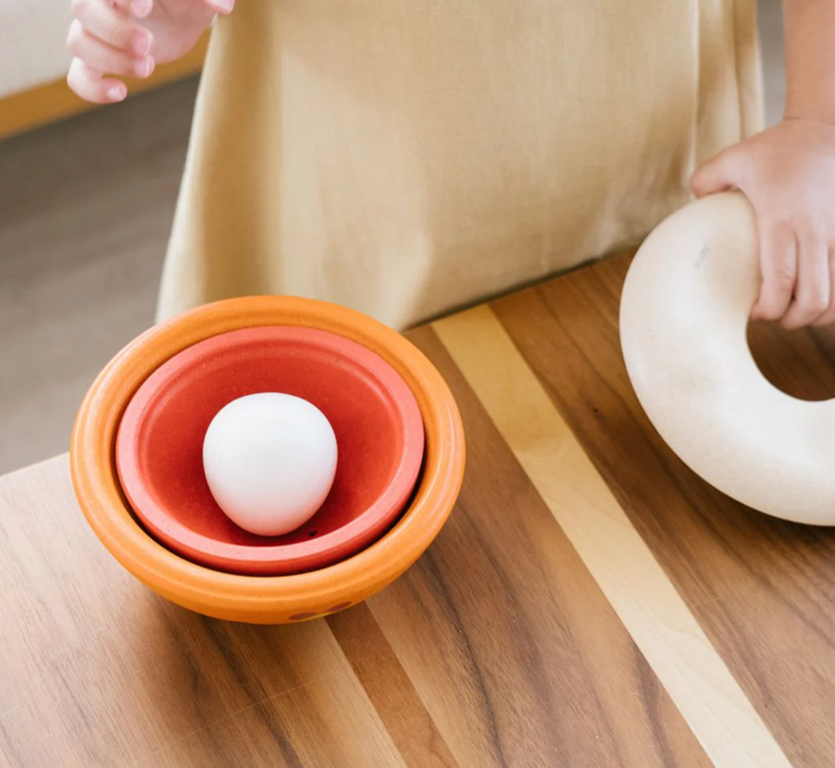 Child playing with Chicken Nesting toy featuring 4 stackable pieces and a nesting base on a wooden table.