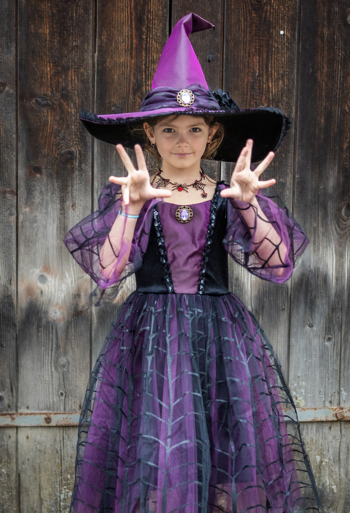 Amethyst the Spider Witch dress with hat in deep purple featuring spiderweb patterns worn by a child posing magically.