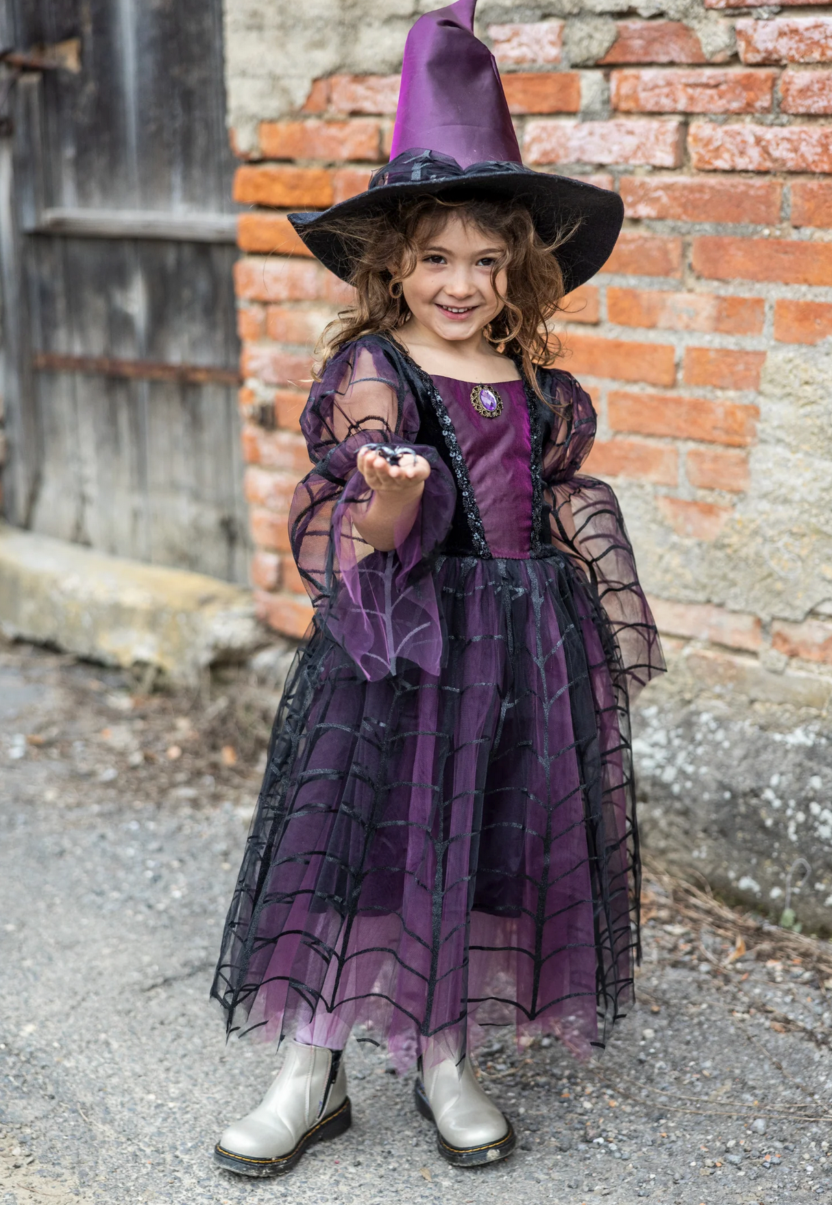 Smiling child in Amethyst the Spider Witch dress and hat with spiderweb pattern and purple accents outdoors.