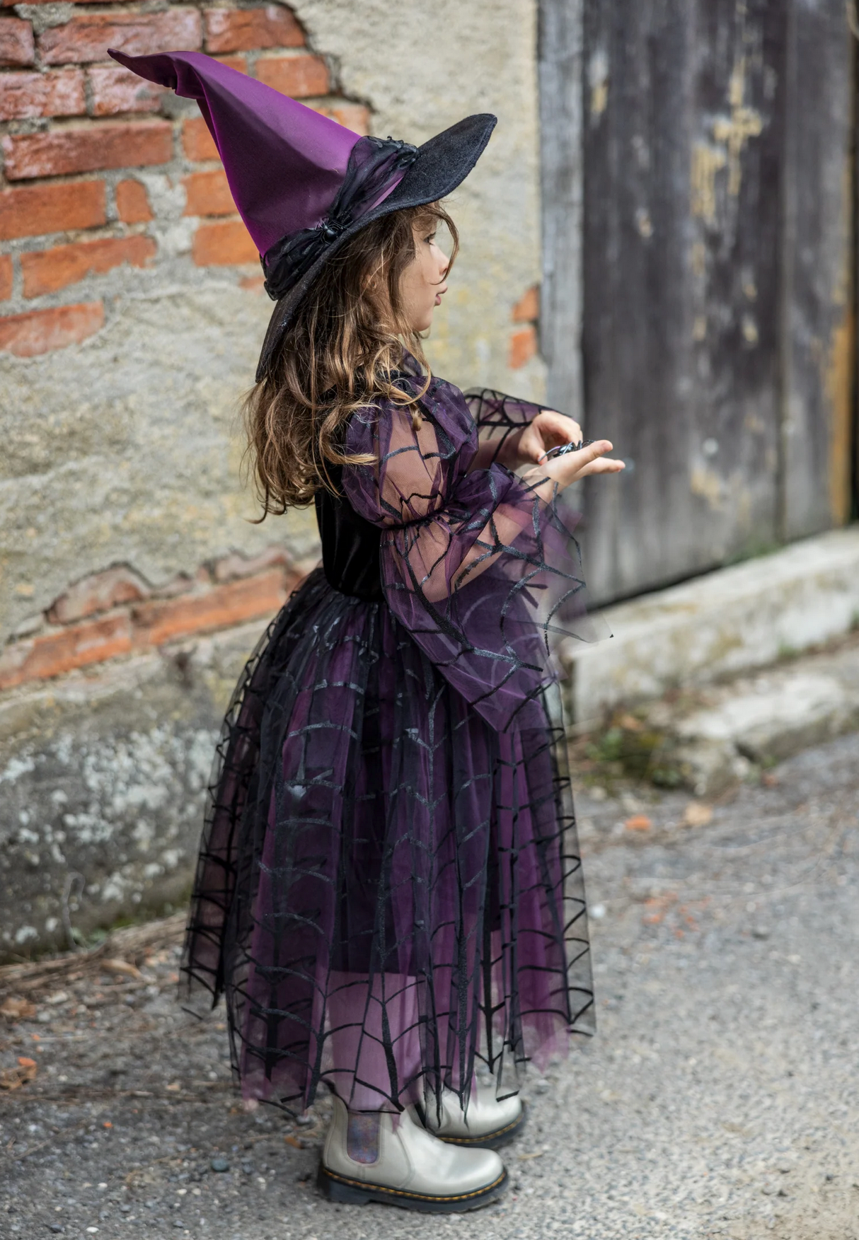 Child dressed in Amethyst the Spider Witch costume with a purple spiderweb dress and matching pointed hat outdoors.