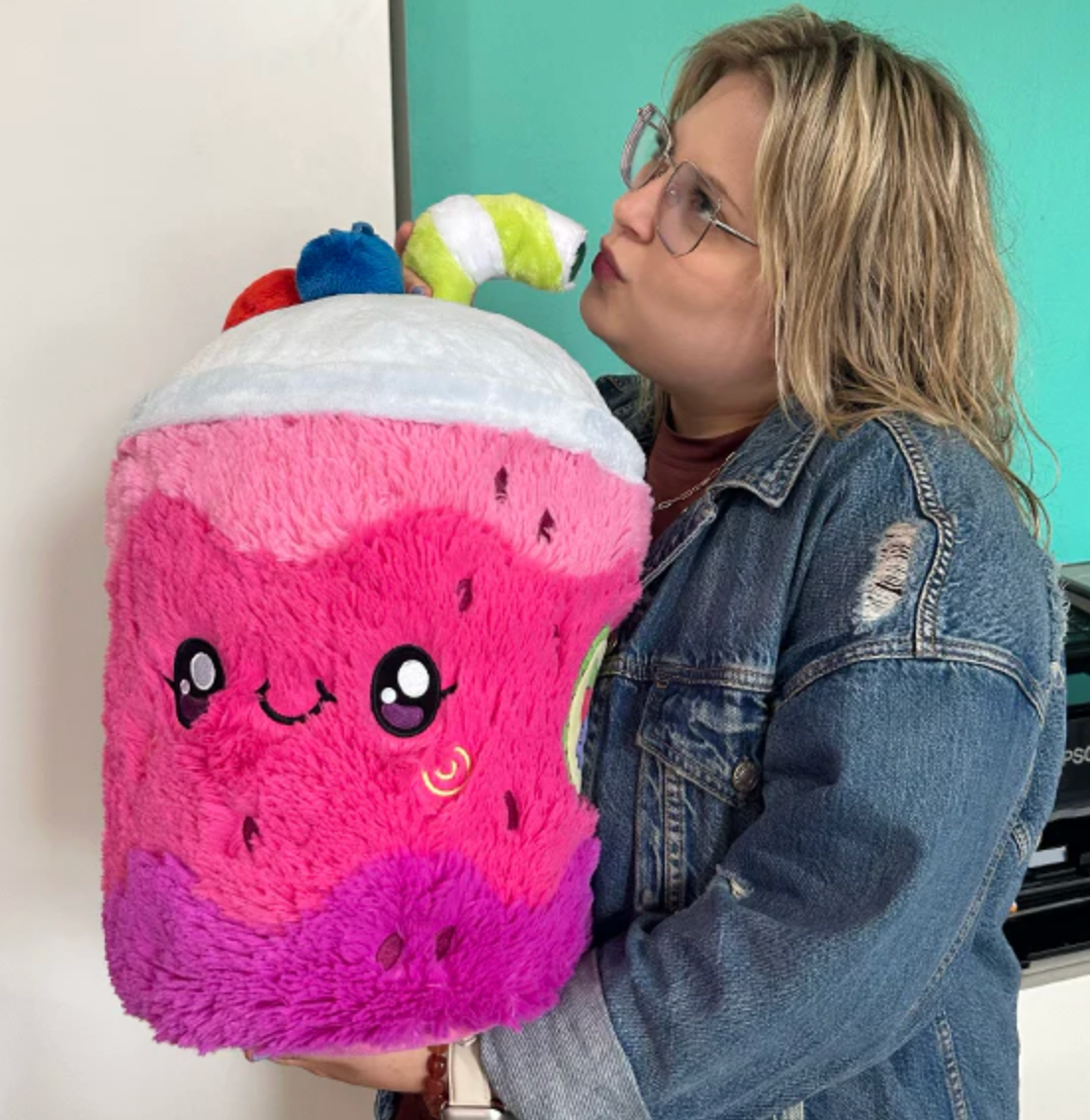Person holding and kissing a large plush toy called Smoothie, designed like a colorful smiling drink with a straw.