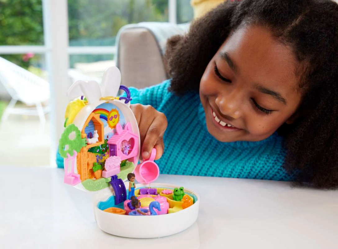 Girl playing with Polly Pocket Bunny World compact featuring water play, tree house, swing, and colorful accessories.