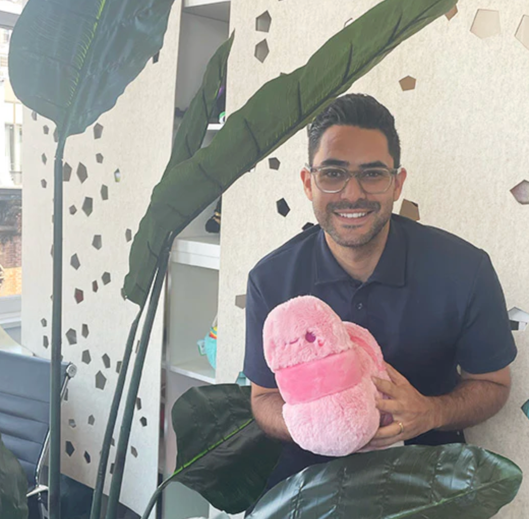 Man smiling and holding a soft pink plush toy Worm Mini in a cozy, modern room setting.