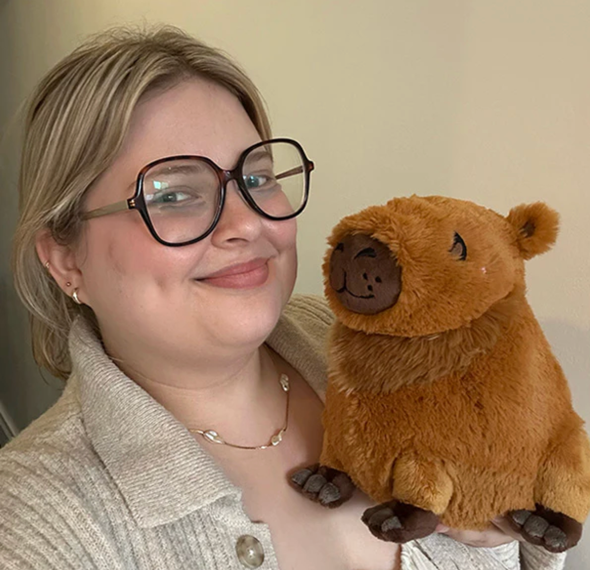 Smiling woman holding a plush Capybara Mini, a soft and cuddly stuffed animal toy, perfect for all ages.