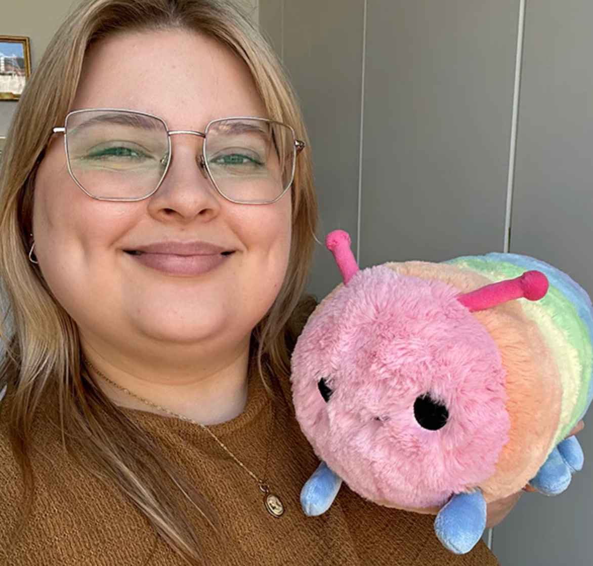 Smiling woman holding Rainbow Caterpillar Mini plush with colorful rainbow stripes and soft texture.