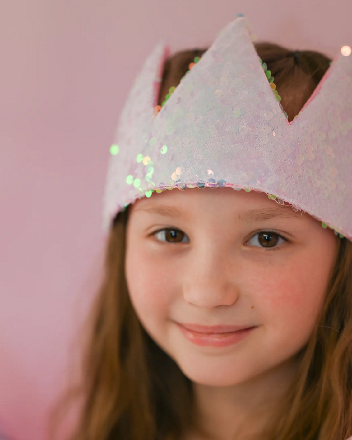 Ombre Sequins Crown with shimmering sequins and soft satin lining worn by a smiling child against a pink background.