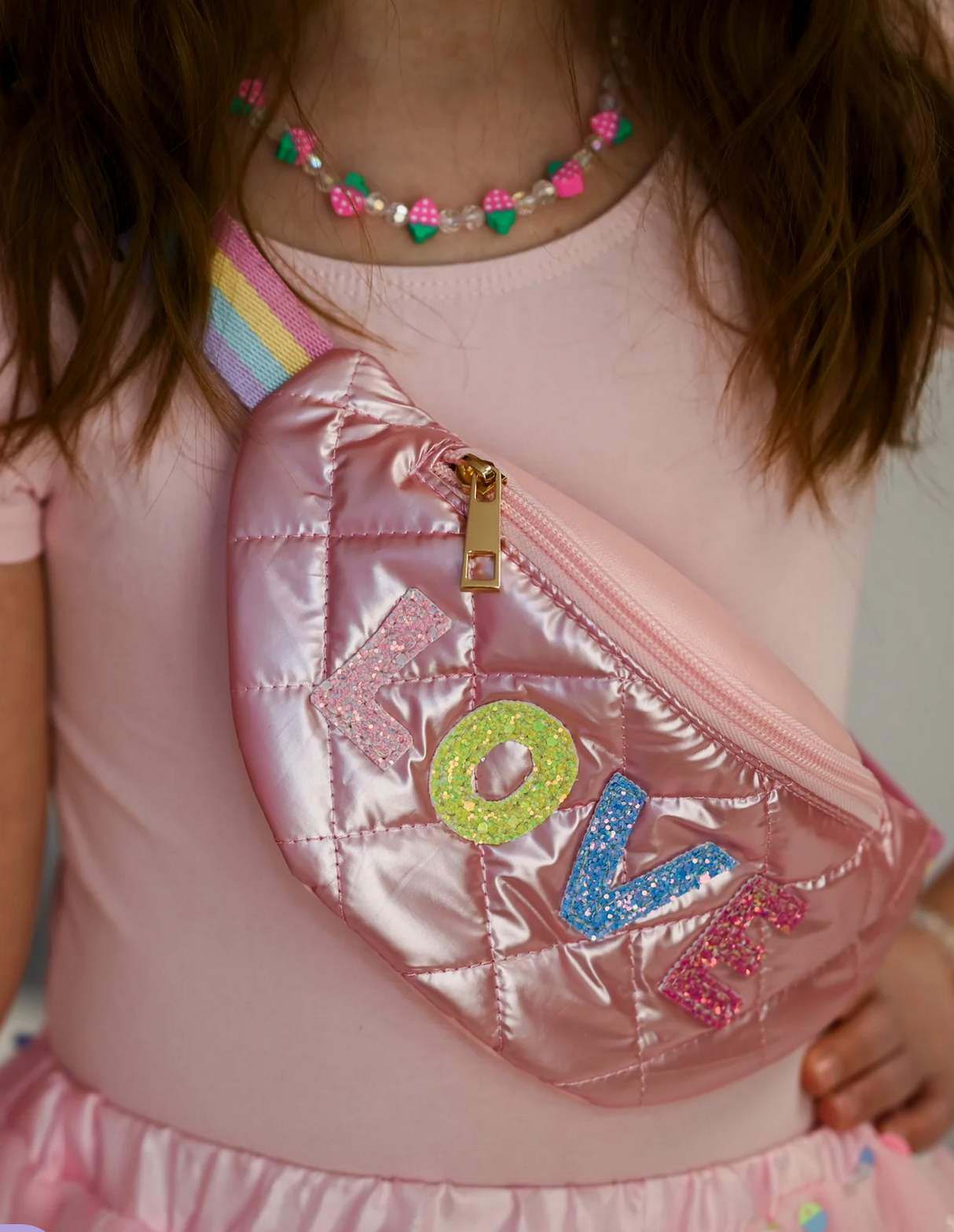 Plushie Love Fanny Pack pink quilted bag with colorful LOVE letters worn by child with rainbow strap.