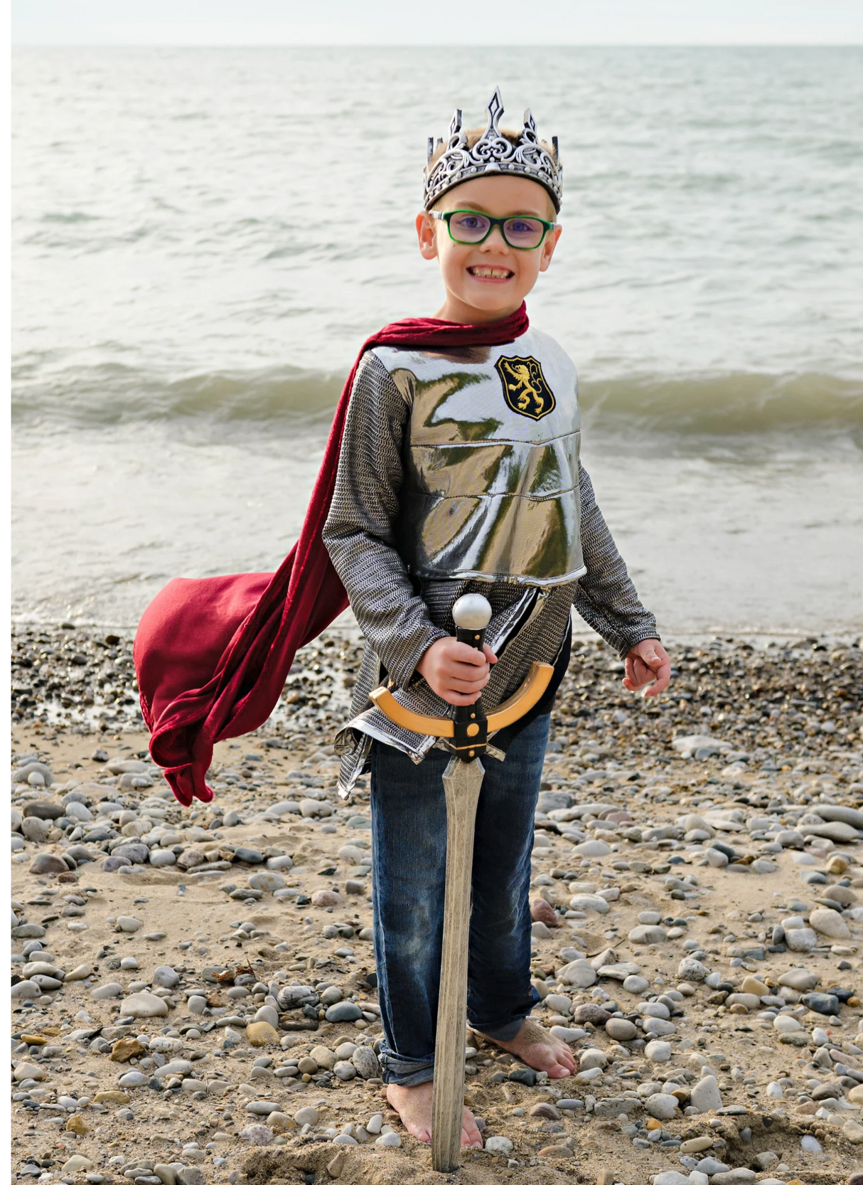 Boy wearing Silver Knight with Cape costume holding a sword on a rocky beach with ocean in the background