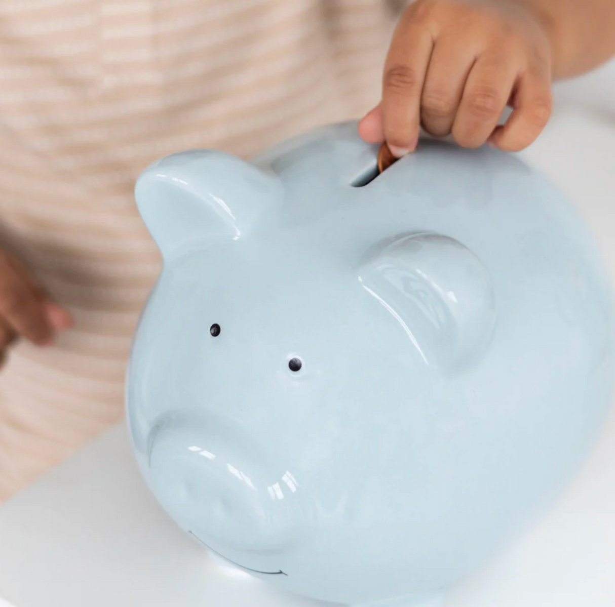 Ceramic Piggy Bank | Blue being used by child to save money, featuring smooth glazed finish and cute design.