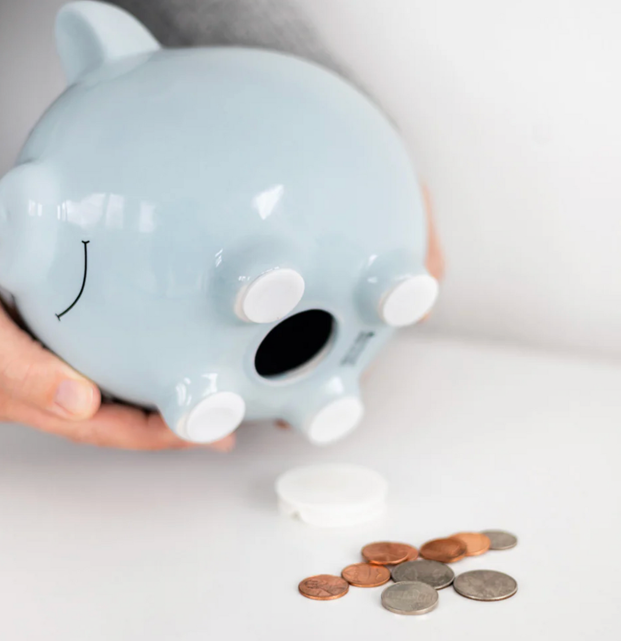 Ceramic Piggy Bank | Blue with removable rubber stopper and felt feet shown with coins and hand holding it.