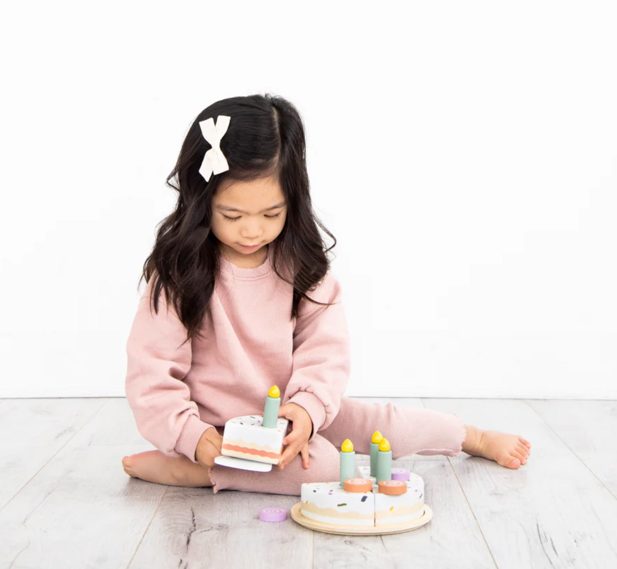 Young girl playing with the Celebration Wooden Cake Set, featuring removable slices, candles, and plate for imaginative play.