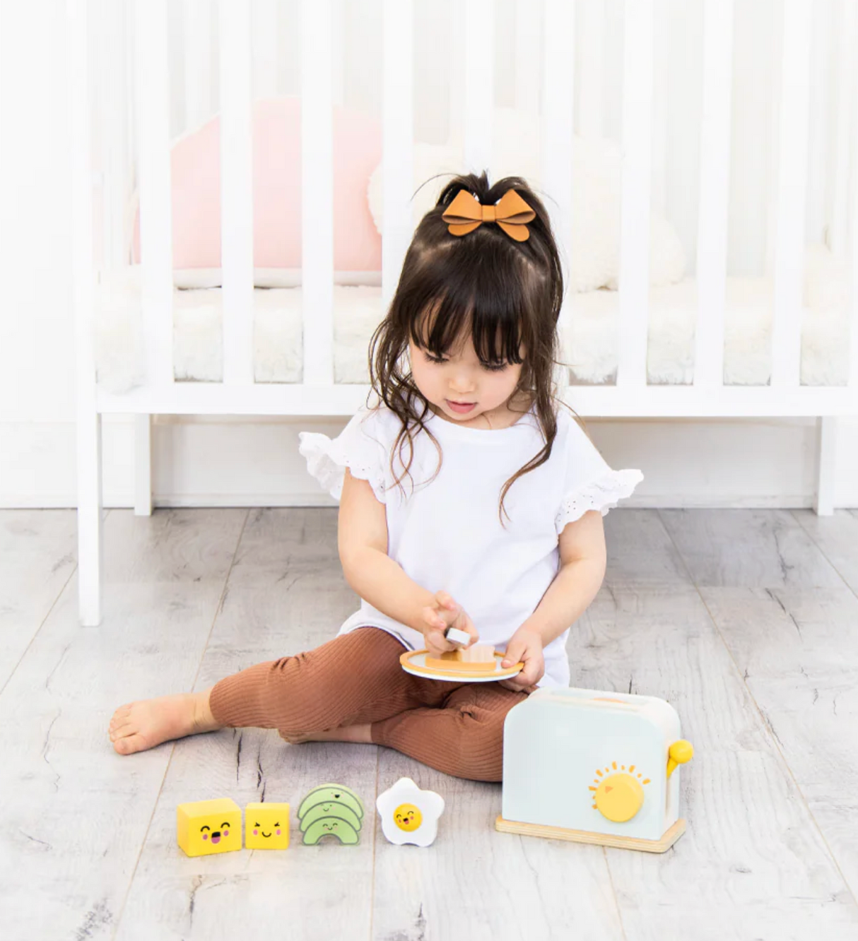 Child playing with Brunch Time Wooden Toaster Set including toaster, toast, and breakfast pieces on floor.