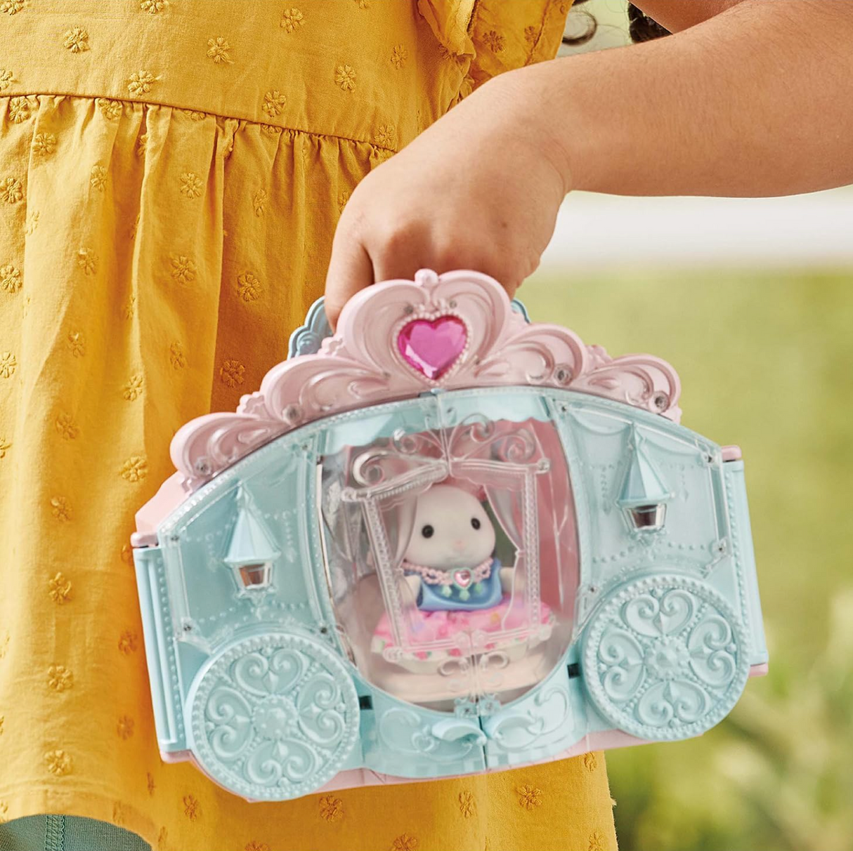 Child holding the Style & Sparkle Dressing Room carriage toy with Snow Rabbit girl figure inside and handle for carrying.