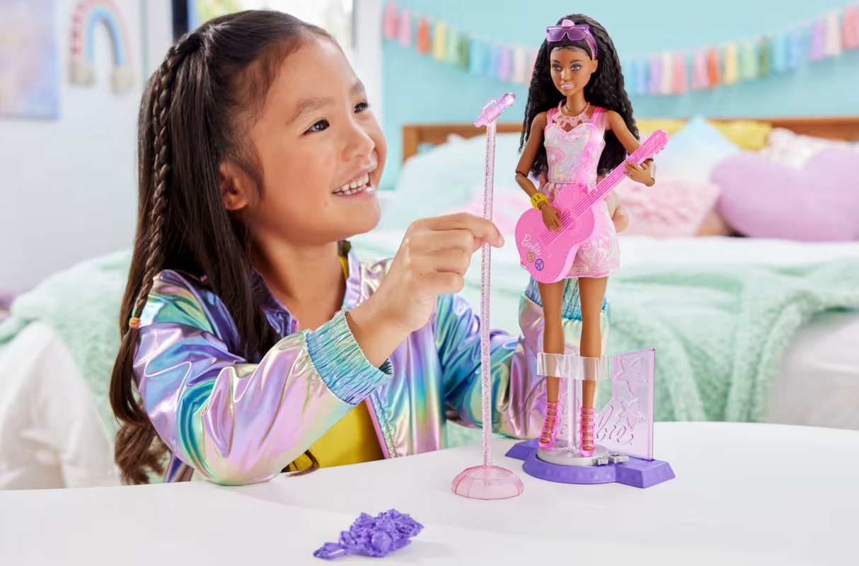 Young girl playing with Barbie Pop Star Playset featuring Barbie doll with pink guitar and rotating stage accessories.