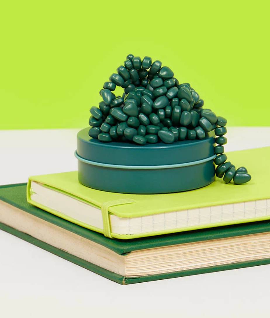 Speks. Matte. Mini Crags. Jade. magnetic putty in a teal tin on stacked green notebooks with a green background.