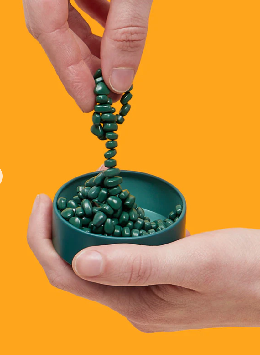 Speks. Matte. Mini Crags. Jade. showing green magnetic putty being stretched from a small teal tin on orange background.