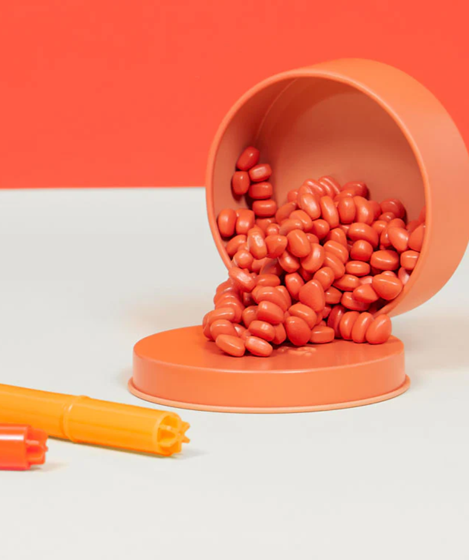 Speks. Matte. Mini Crags. Coral. small coral magnetic putty pieces spilling from an open round tin container.