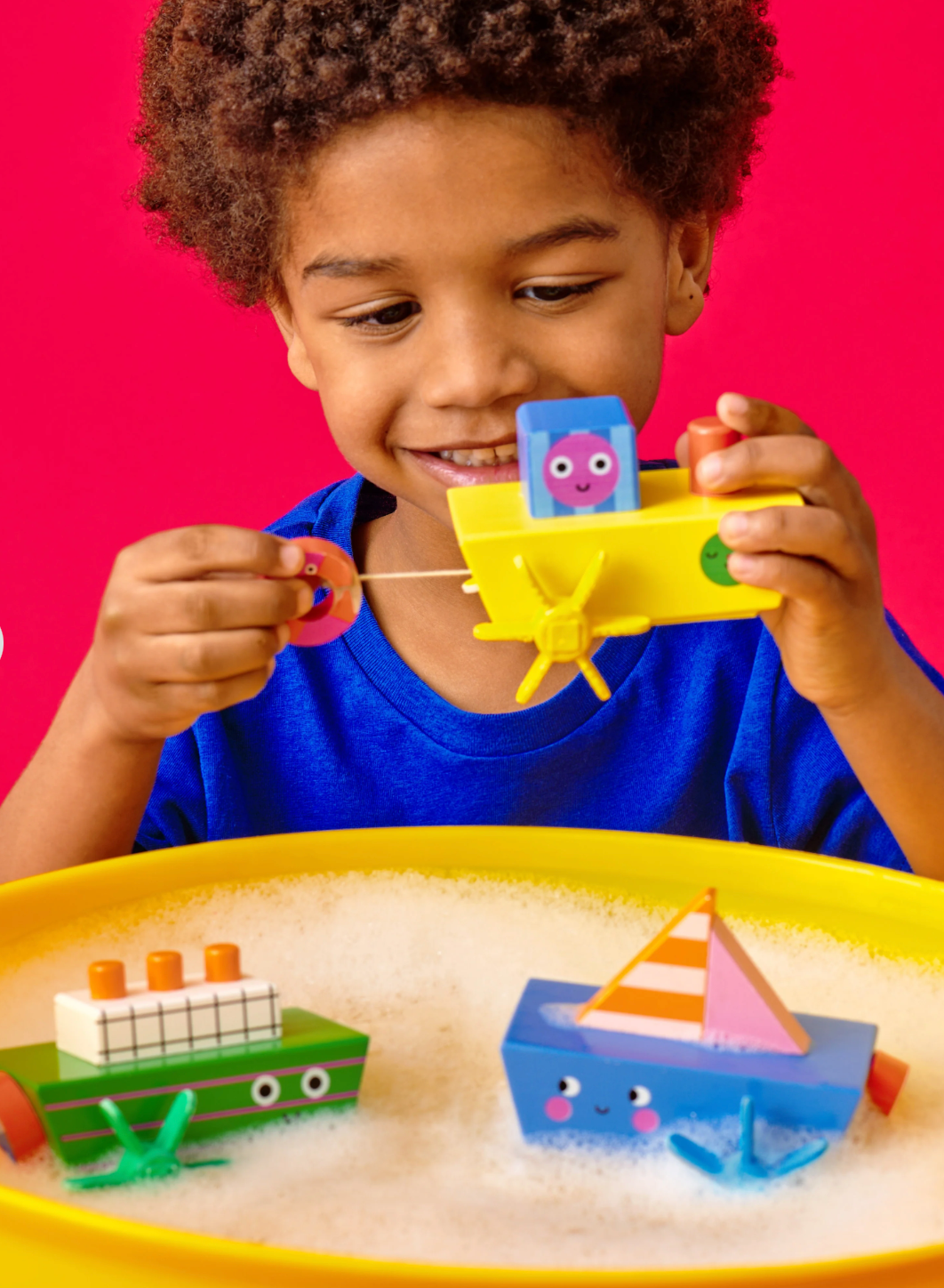 Child playing with a yellow Kidoki Windup Boat in a bubbly water tray for interactive bath time fun