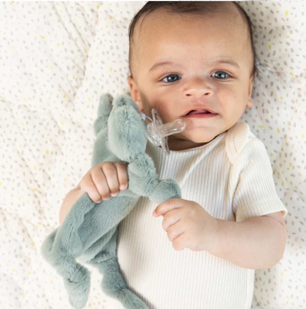 Baby holding Freddie the Frog Pacifier Buddy with attached pacifier, soft plush lovey for infants 0 months and up.