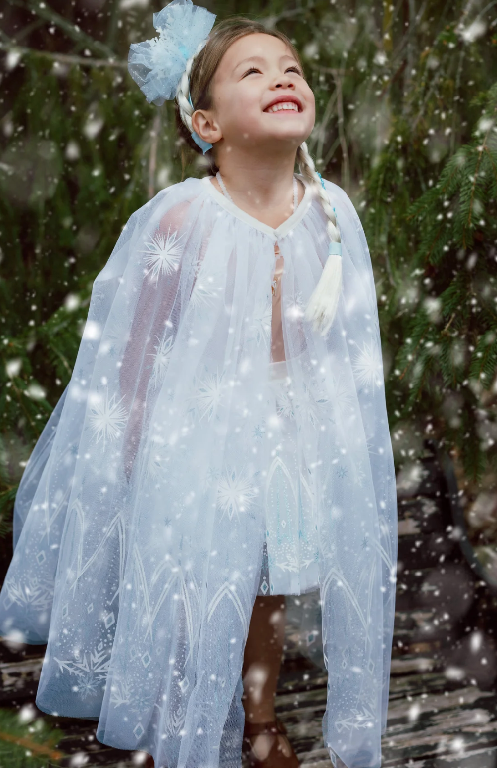 Smiling child wearing Winter Wonderland Tutu with snowflake cape and blue hair accessory in snowy outdoor setting.