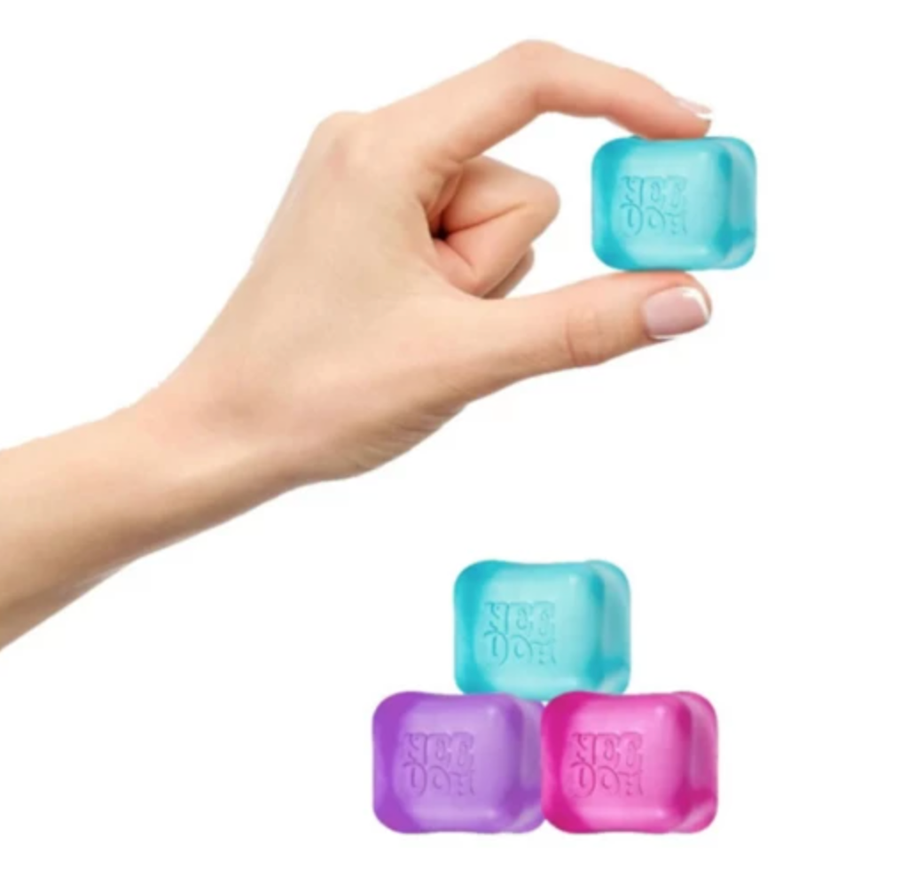Hand holding a blue NeeDoh Nice Ice Baby fidget toy above purple and pink cubes on white background.