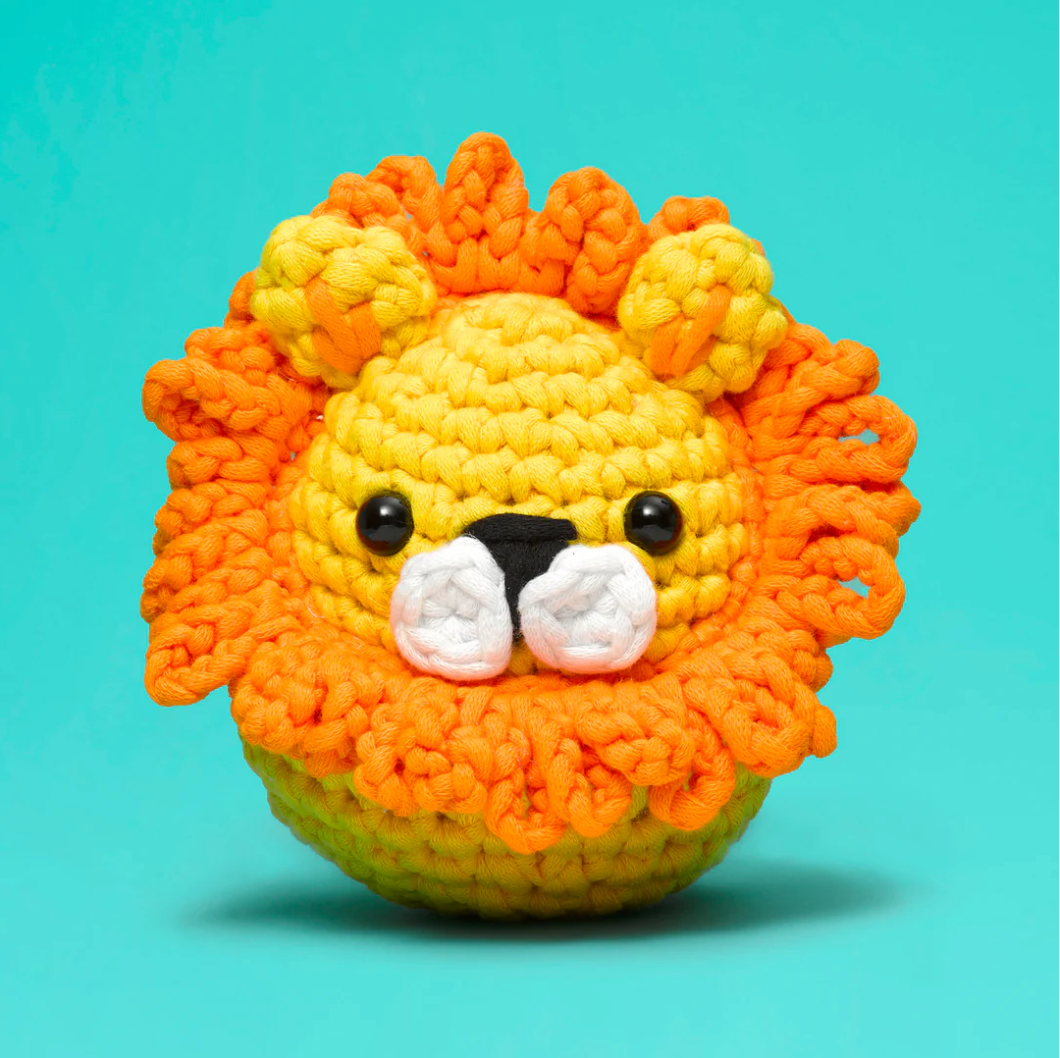 The Woobles Crochet Kit | Sebastian the Lion, a cute handmade crocheted lion with a bright orange mane on blue background.