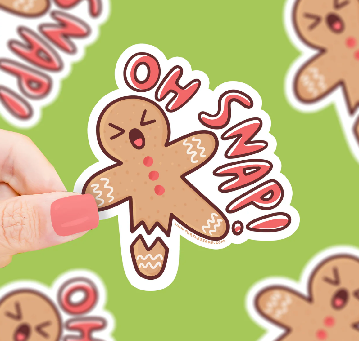 Hand holding an Oh Snap! Gingerbread Man Sticker with a cracked gingerbread man and red text on a green background.